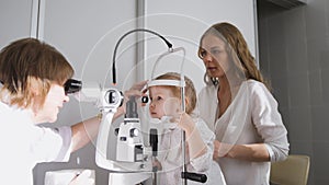 Little girl and her mommy in ophthalmology - optometrist checking little child`s vision