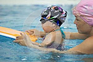 Little girl and her mother making excercises with float board in the swimming pool