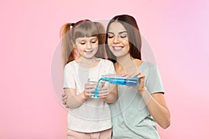 Little girl and her mother with mouthwash on color background