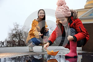 Little girl and her mother playing with paper boat near puddle outdoors