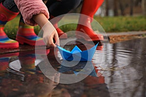 Little girl and her mother playing with paper boat near puddle outdoors, closeup