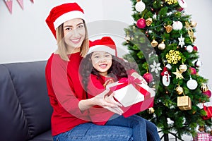 Little girl and her mother wearing santa hat holding christmas gift box and smile at home