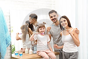 Little girl and her parents brushing teeth together in bathroom at home