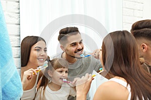 Little girl and her parents brushing teeth together near mirror in bathroom