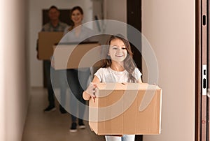Little girl and her parents with cardboard boxes indoors. Moving into new apartment