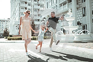 Little girl and her parents skipping along the street.