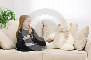 Little girl with her white teddy bear having conversation on the sofa.