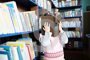 Little girl hide behind book in library environment