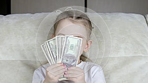 A little girl hides behind a money fan of one hundred dollar bills