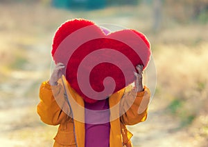 Little girl hiding behind heart shaped pillow