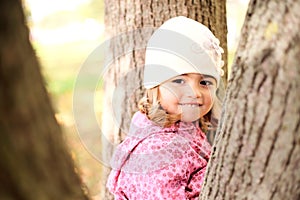 Little girl hiding in the trees in autmn park