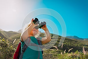 Little girl hiking in mountains looking at binoculars