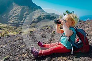 Little girl hiking in mountains looking at binoculars