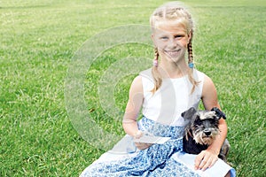 Little girl with his dog sitting on green grass and read e-book.