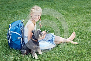 Little girl with his dog sitting on green grass and read e-book.