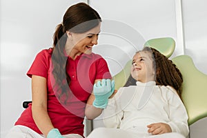 Little girl holding an artificial model of human jaw with dental braces in orthodontic office, smiling. Pediatric