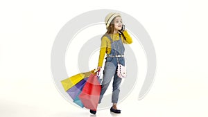 Little girl holding bags and talking on the phone, smiling. White background. Slow motion