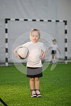 A little girl holding the ball in one hand on the football field, looking at the camera