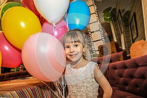 Little girl holding balloons. The child smiles cheerfully on a holiday.