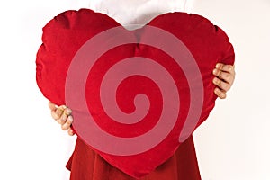 Little girl holding big red heart on her hands. Girl is wearing white shirt and red skirt.