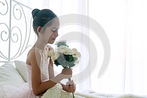 Little girl holding bouquet flower in her hand while sitting on the bed with pillow at home. Adorable children wake up