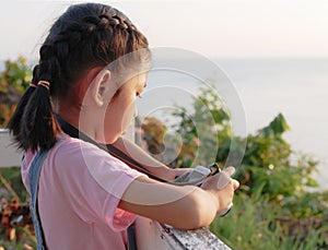 A little girl holding camera with taking a picture. Asian kid making photo in twilight with copy space