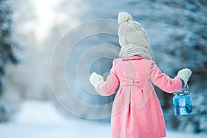 Little girl holding Christmas lantern outdoors on beautiful winter snow day