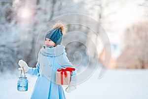 Little girl holding Christmas lantern and present on New Year outdoors on beautiful winter snow day