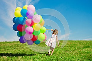 Little girl holding colorful balloons. Child playing on a green