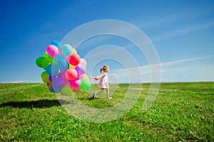 Little girl holding colorful balloons. Child playing on a green