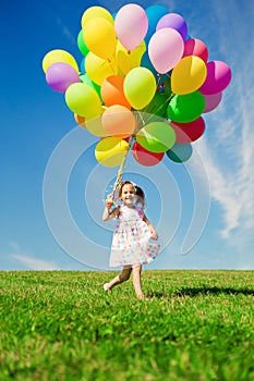 Little girl holding colorful balloons. Child playing on a green