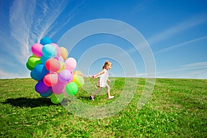 Little girl holding colorful balloons. Child playing on a green