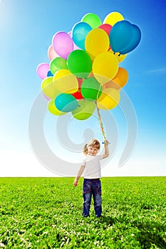 Little girl holding colorful balloons. Child playing on a green