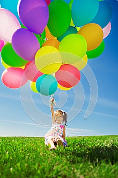 Little girl holding colorful balloons. Child playing on a green