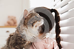 Little girl holding cute cat near window. First pet