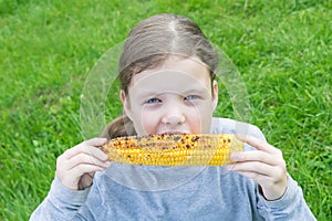 Little girl holding an ear of corn in her hands and wants to eat it, looking forward