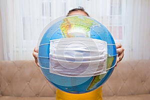 The little girl is holding the earth globe in her hands. Surgical mask on earth globe