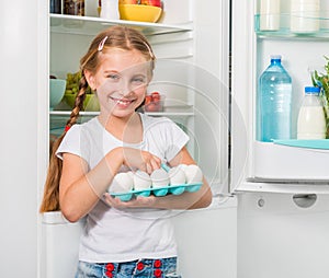 Little girl holding eggs near fridge