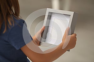 Little girl holding empty photo frame on blurred background, closeup