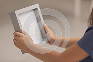 Little girl holding empty photo frame on blurred background, closeup