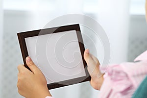 Little girl holding empty photo frame indoors, closeup