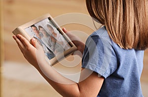 Little girl holding framed family photo, closeup