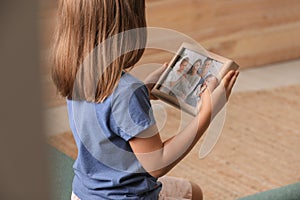 Little girl holding framed family photo indoors, closeup