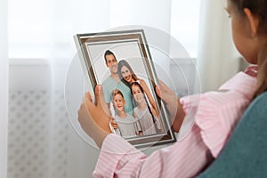 Little girl holding framed family photo indoors, closeup