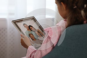 Little girl holding framed family photo indoors, closeup