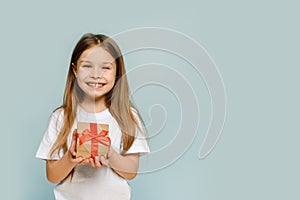 Little girl holding a gift on a blue background with copy space. Looking at camera