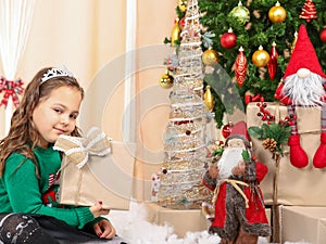 Little girl holding a gift in front of christmas tree