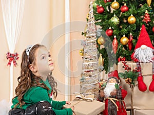 Little girl holding a gift in front of christmas tree