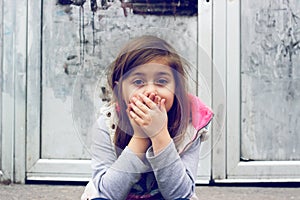 Little girl holding hands over her mouth