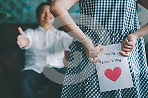 Little girl holding and hiding greeting card for father behind back.Concept of Happy father`s day
